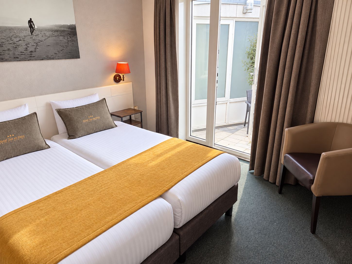 Une chambre d’hôtel avec deux lits, un canapé, une table de chevet, une lampe et une vue sur l’extérieur.