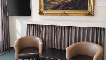 Une chambre d’hôtel avec un tableau, deux chaises, une table, un lit et un téléviseur à écran plat.
