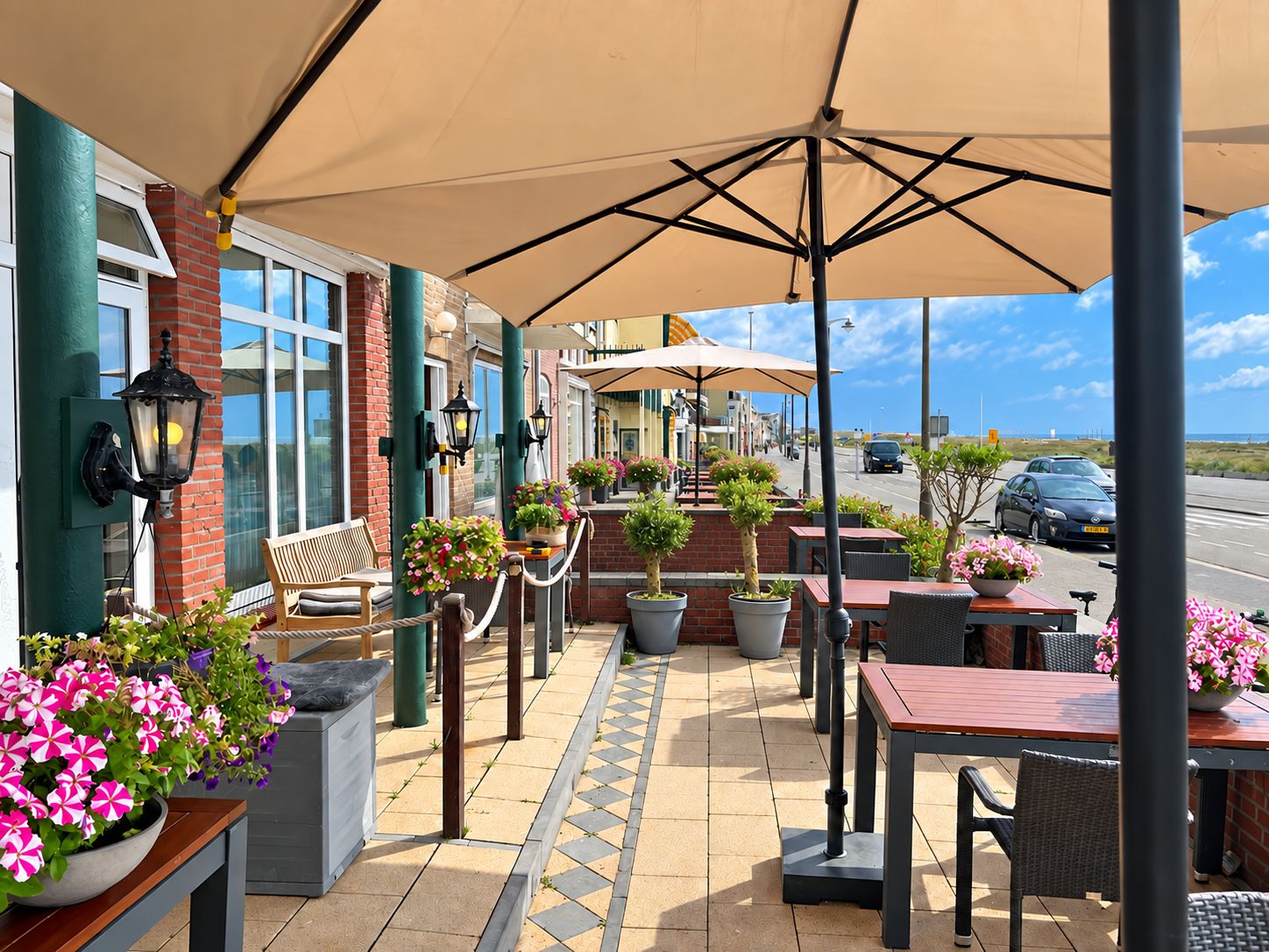 Een terras buiten met tafels en stoelen, potplanten en uitzicht op de straat.