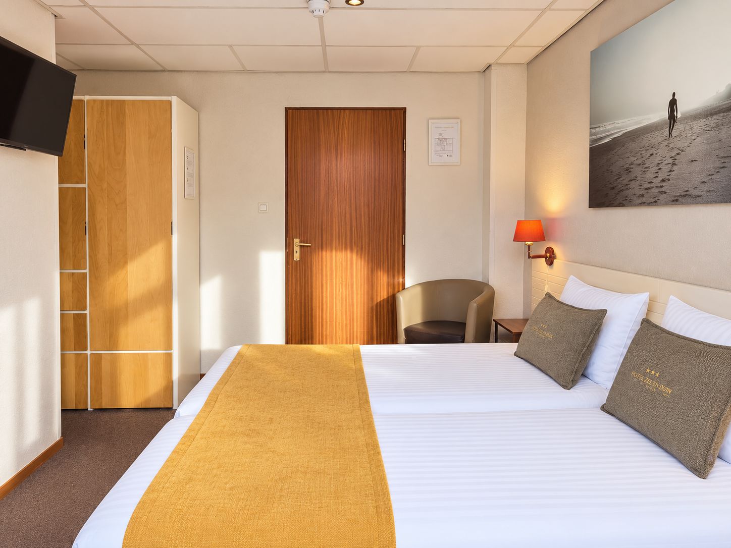 Een hotelkamer met een bed, een bureau, een stoel, een kledingkast, een televisietoestel en een schilderij aan de muur.