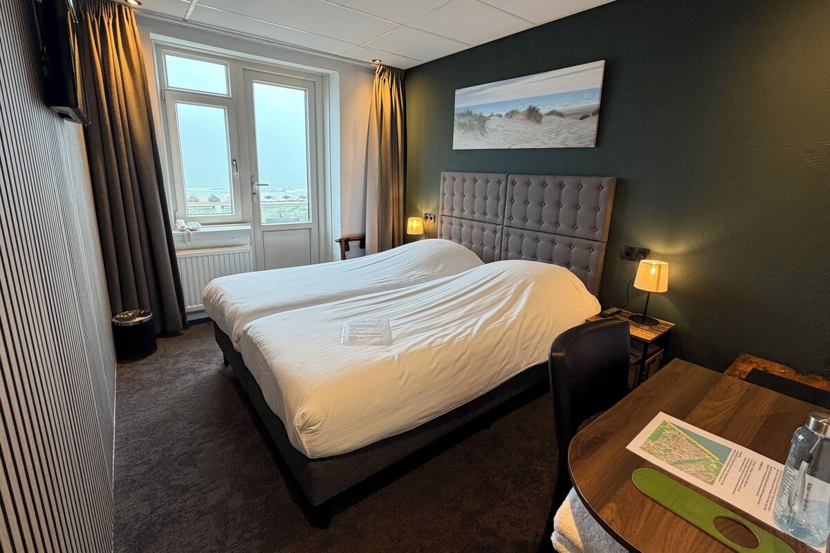Habitación de hotel con una cama grande, un escritorio con lámpara, un cuadro en la pared y vistas por la ventana.