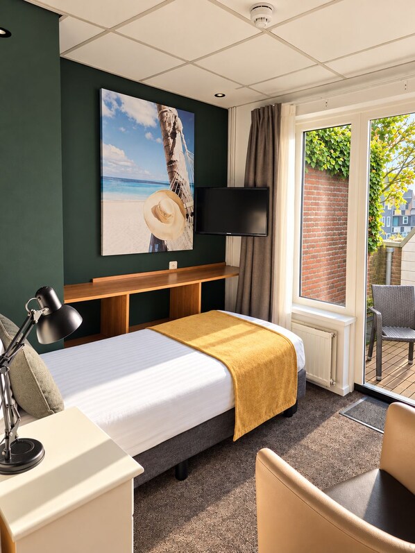 A hotel room with a bed, a desk, a chair, a television, and a window with a view of the outside. - Hotel Zee en Duin (Katwijk Aan Zee)