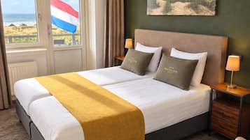 A hotel room with a bed, a view of the beach, and a flag.