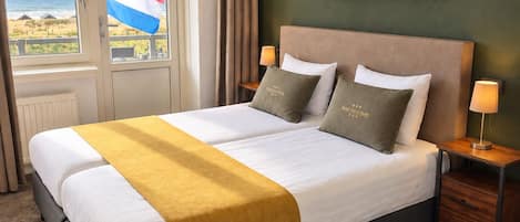 A hotel room with a bed, a view of the beach, and a flag.