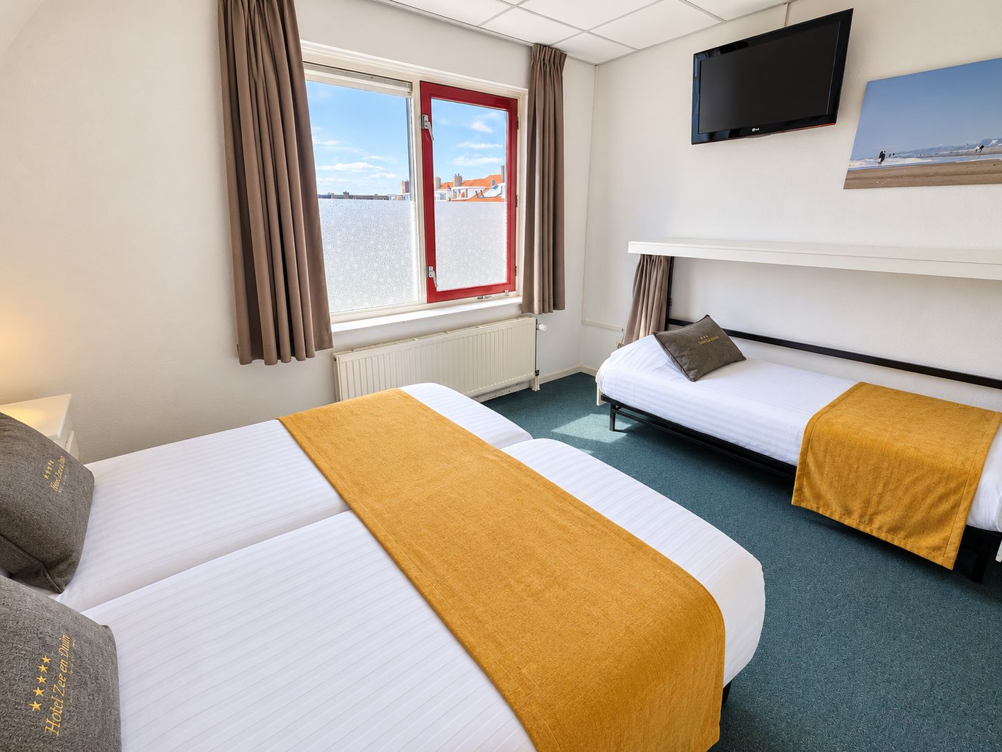 Een hotelkamer met twee bedden, een televisie en een raam met uitzicht op gebouwen.