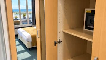 A hotel room with a bed, a mirror, and a shelf with a pillow and a small electronic device.