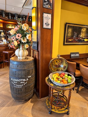 A bar area with a barrel labeled 'GLENROTHL'S' and a decorative chair with a fruit basket. - Hotel Zee en Duin (Katwijk Aan Zee)