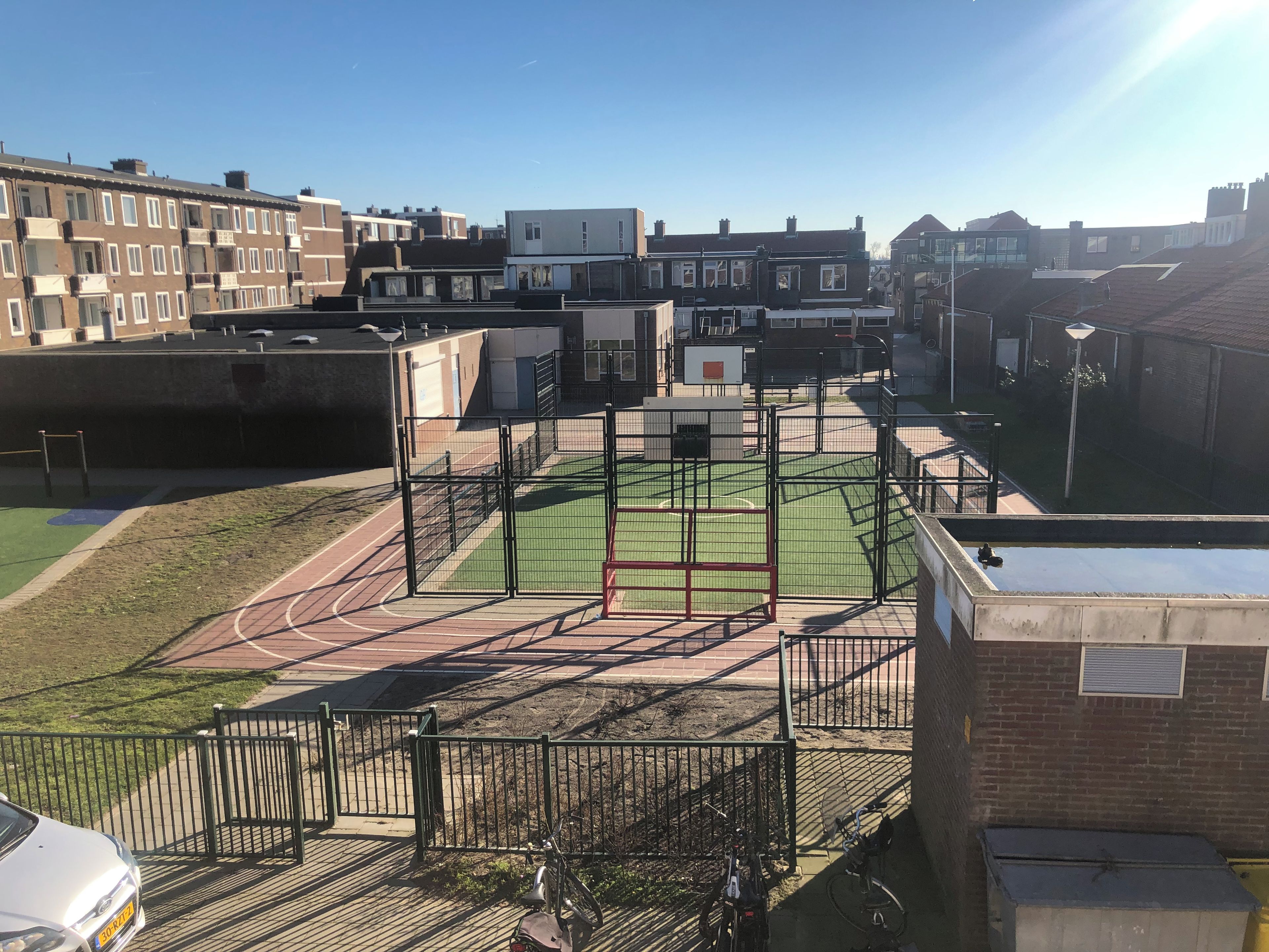 Een sportveld met een atletiekbaan en een omheind gebied, omringd door woongebouwen.