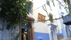 Une rue étroite bordée d’un immeuble sur lequel on peut lire l’inscription : « Hôtel Dar Chechouen ».