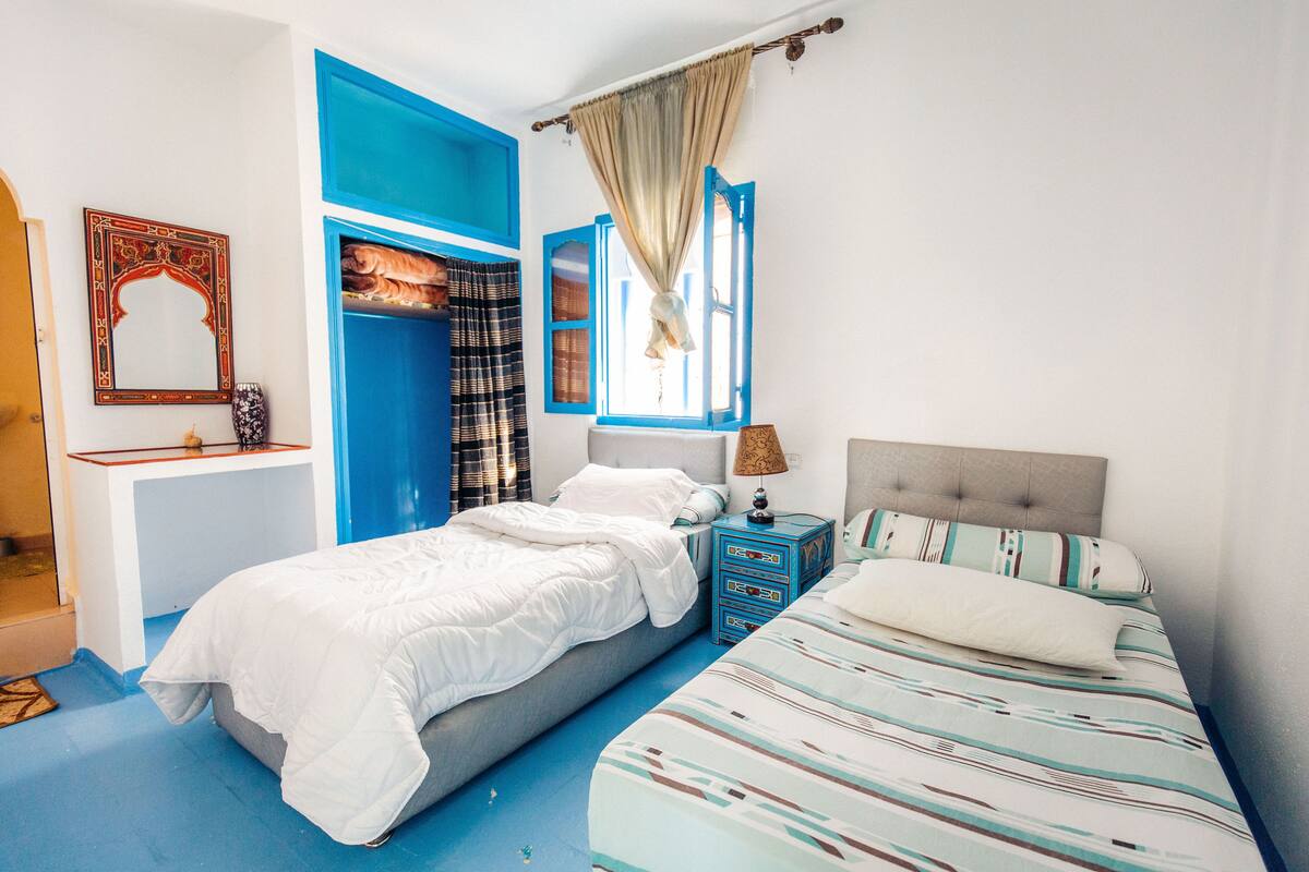 Une chambre à coucher avec un lit, une table de chevet, une commode et une fenêtre avec des rideaux.