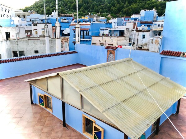 Una terraza en la azotea con techo de metal corrugado, paredes azules y piso de baldosas.