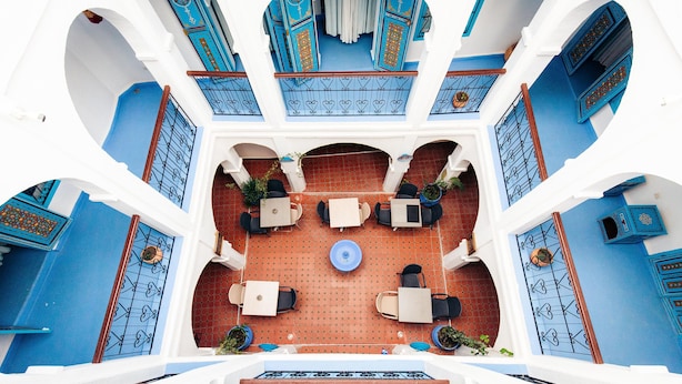 Une cour intérieure avec un espace de repos central, entourée de portes bleues et de murs blancs.