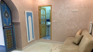 Une pièce comprenant un lit, un canapé beige, une porte bleue ornée de motifs complexes et donnant sur une salle de bain.