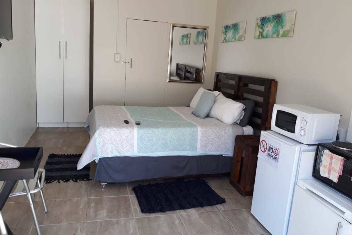 Un dormitorio con cama, escritorio, armario, espejo y kitchenette con microondas.