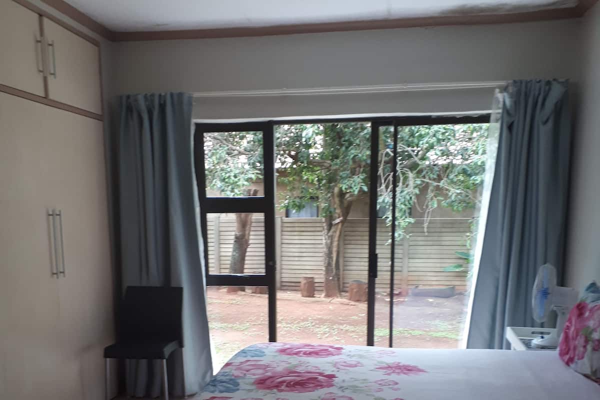 Un dormitorio con cama, una silla, un armario y un ventanal corredera que da a un espacio exterior.
