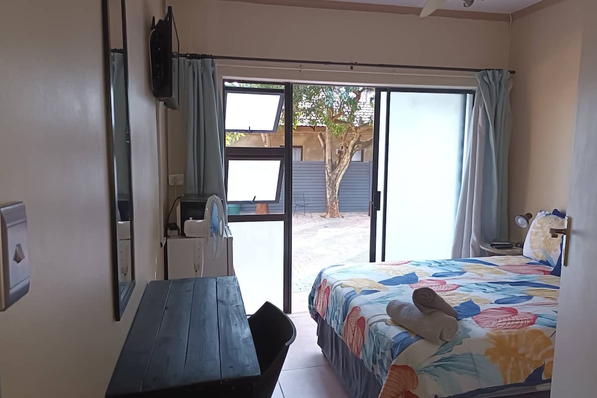 Habitación de hotel con cama, escritorio, silla, televisor y ventana con cortinas.