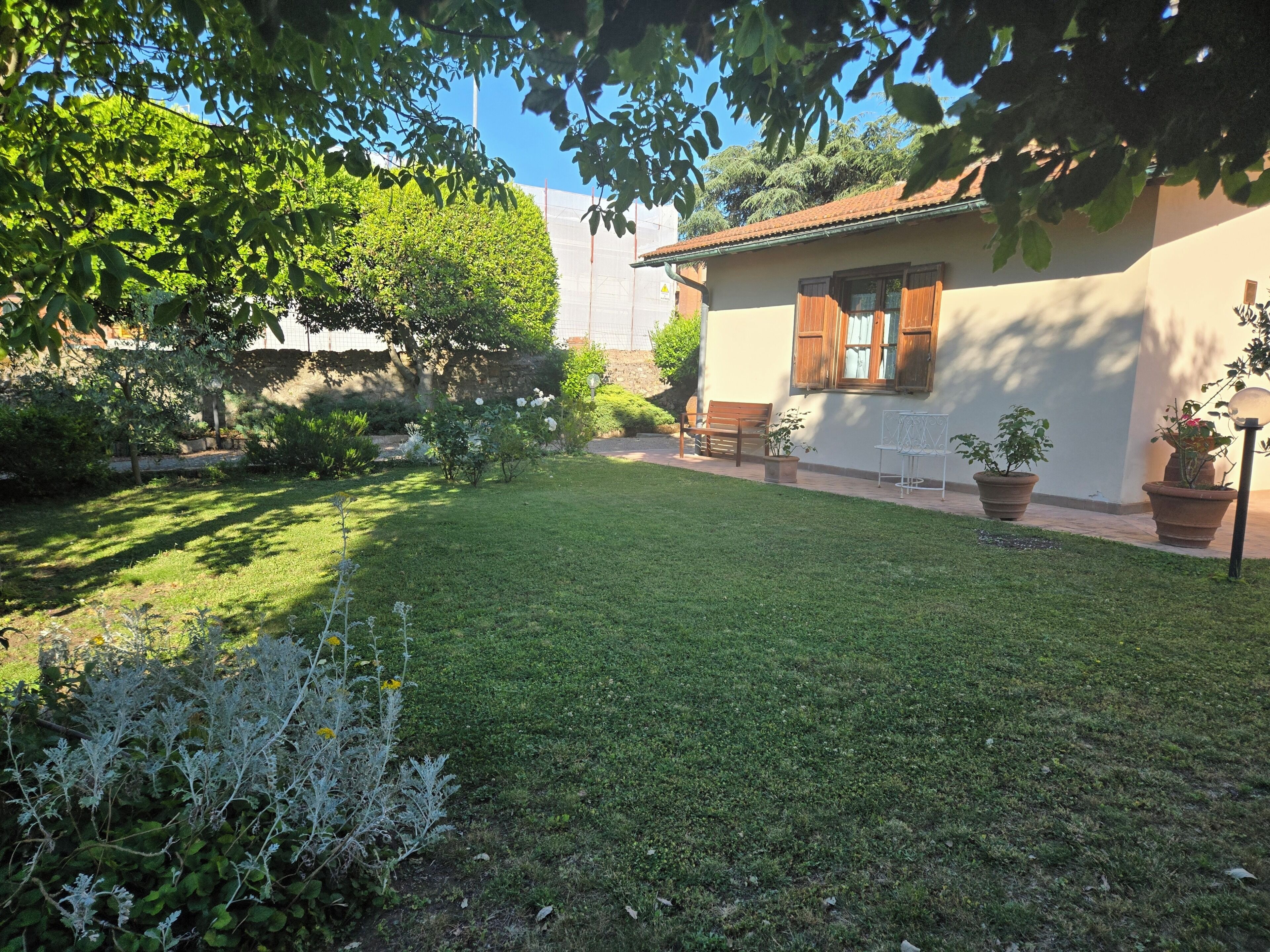 Un jardin bien entretenu, avec une pelouse, des plantes en pot et un bâtiment doté d’un toit en tuiles.