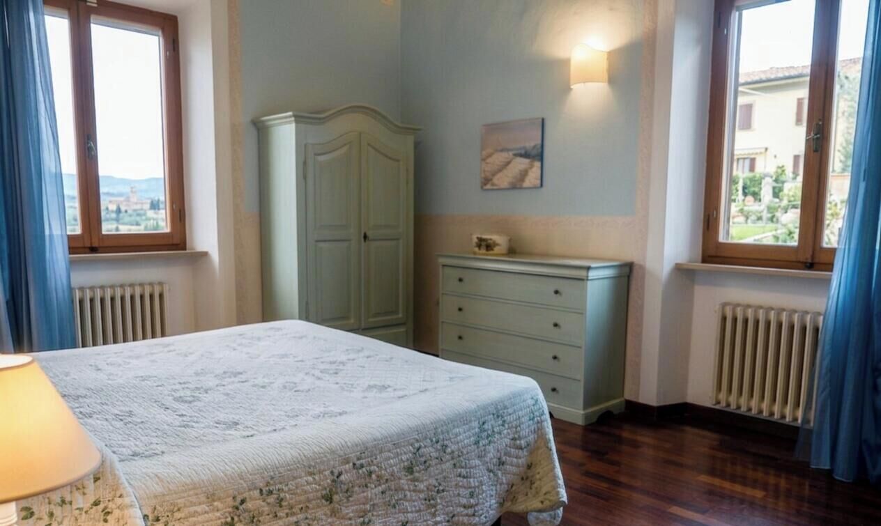 Une chambre à coucher avec un lit, une commode, un radiateur et une fenêtre avec des rideaux.