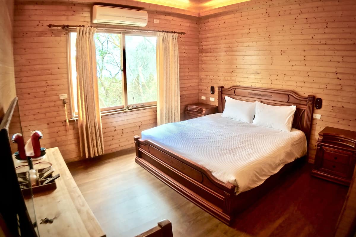 A wooden-paneled bedroom with a bed, a desk, and a window with curtains.