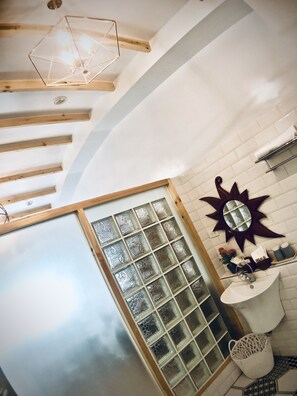 A bathroom with a white tiled wall, a star-shaped mirror, a white sink, and a window with frosted glass panels.