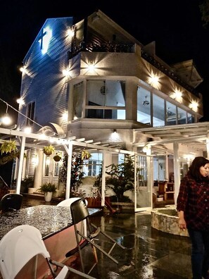 A two-story building with a prominent cross on the facade, large windows, and a covered outdoor area with chairs and a table.