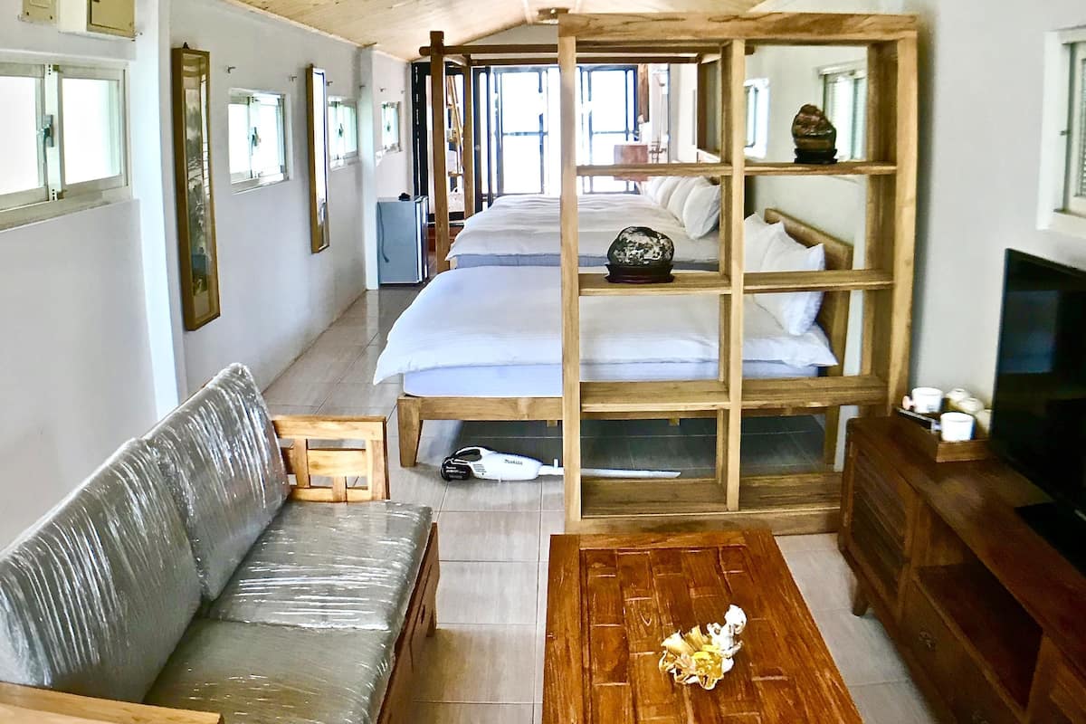 A room with a wooden ceiling, a bed with a wooden frame, a sofa, a wooden coffee table, and a television.