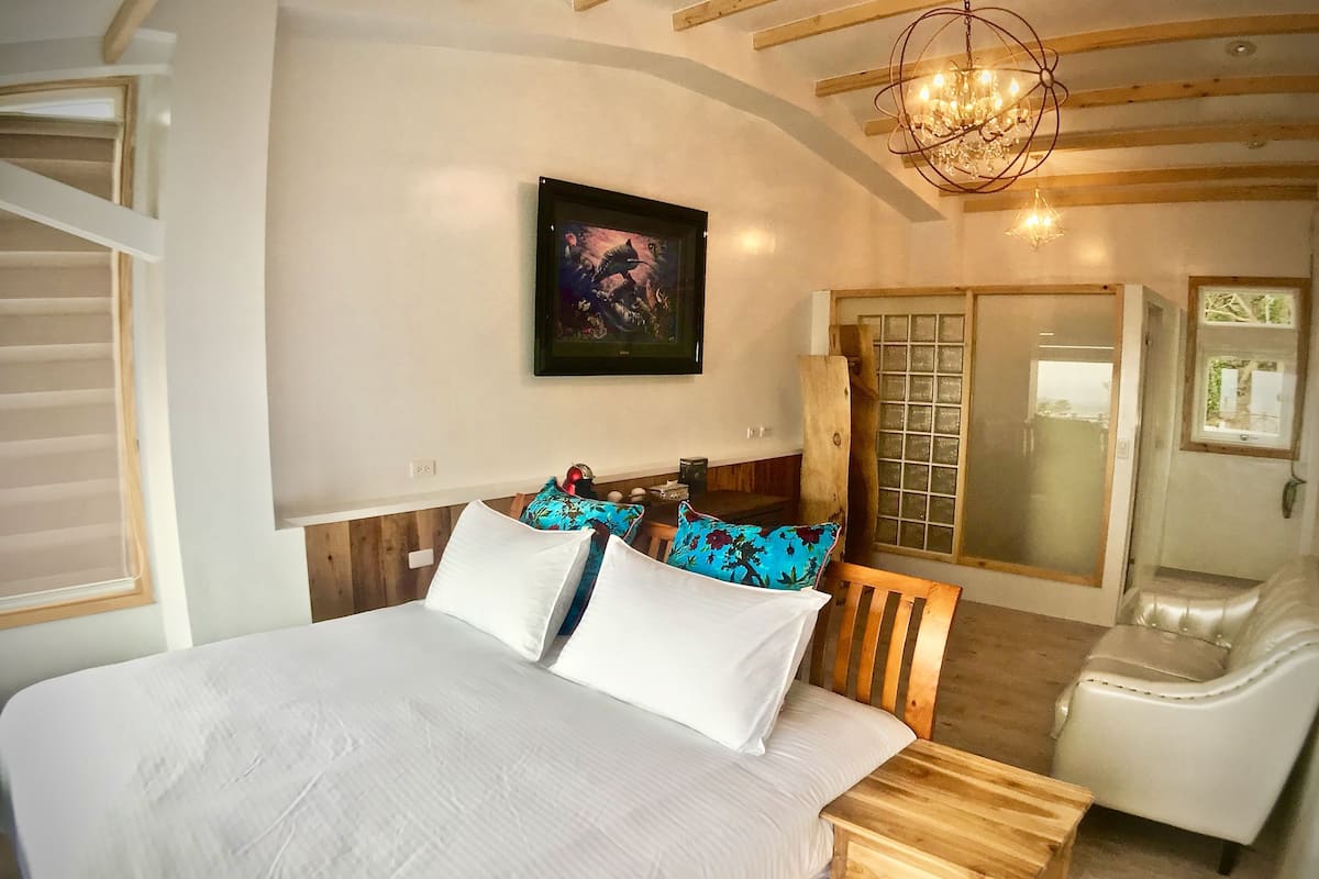 A bedroom with a large bed, a wooden nightstand, a chair, a mirror, and a chandelier.