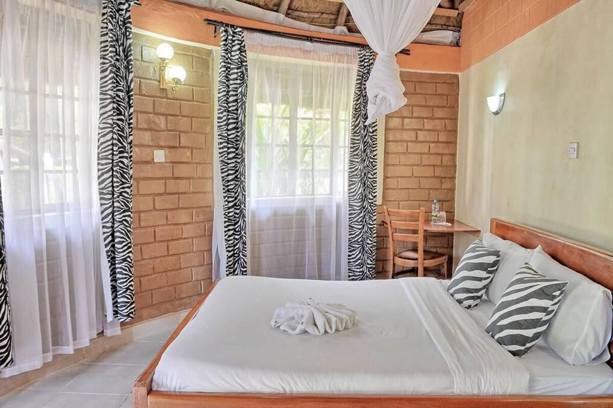Quarto com cama, cortinas com padrão de zebra, cabeceira de madeira e uma pequena mesa com uma cadeira.