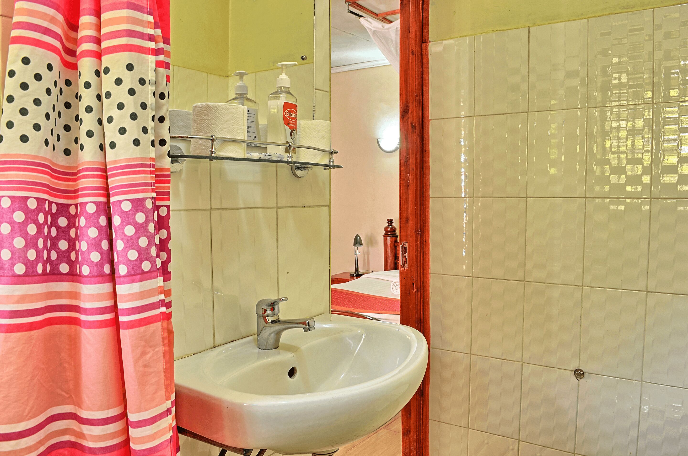 Un baño con lavamanos blanco, un espejo y un estante con artículos de aseo.