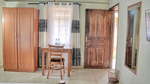 Une pièce avec une armoire en bois, une table à manger avec deux chaises, une fenêtre avec des rideaux à motifs et une porte en bois.