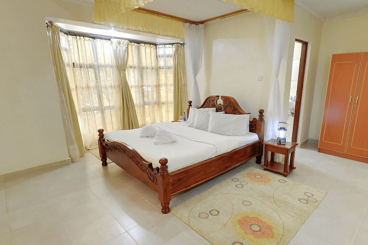 Quarto com cama de madeira, mesa de cabeceira com abajur, guarda-roupa e janela com cortinas.