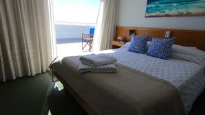 A hotel room with a bed, a nightstand, a chair, and a painting of the ocean. - Hotel Solmar (San Clemente)