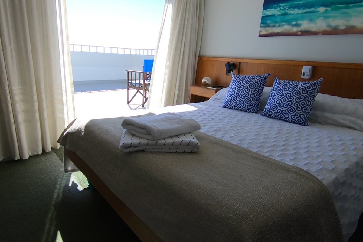 Una habitación de hotel con una cama, una mesita de noche, una silla y un cuadro del océano.