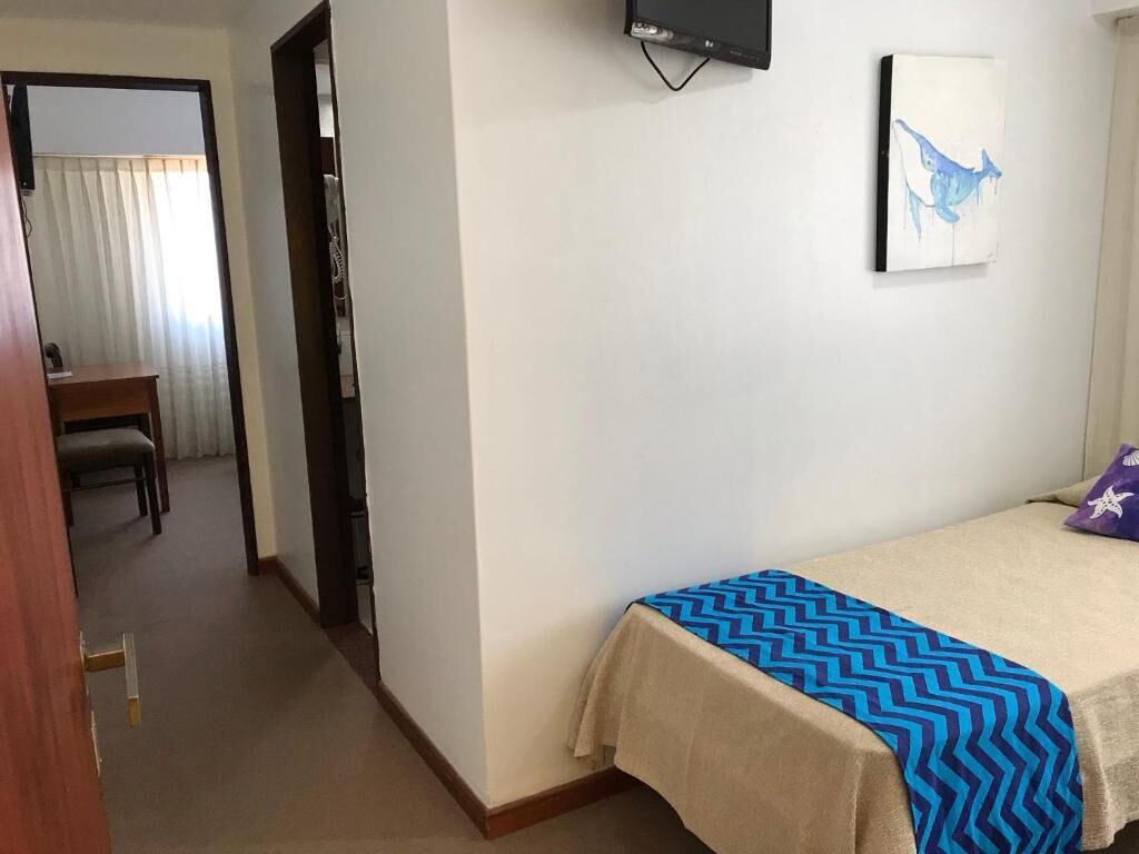 A hotel room with a bed, a TV mounted on the wall, and a painting.