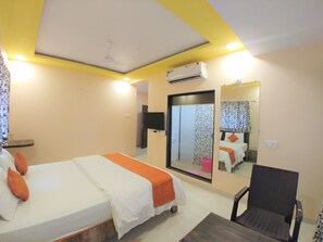 A hotel room with a bed, a chair, a desk, a mirror, an air conditioning unit, and a wardrobe. - Hotel Mangal Residency (Mawal)