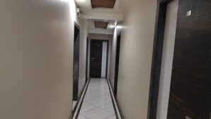 Um corredor estreito e revestido com azulejos, com uma porta escura à direita e uma parede clara à esquerda.