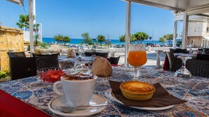 Mesa exterior con vista al mar, una taza de café, un vaso de jugo de naranja y un pastel.