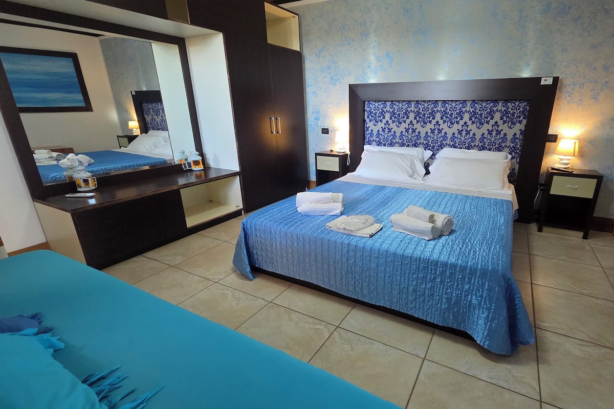 A hotel room with a large bed, a bedside table, a nightstand, a mirror, and a bathroom area.
