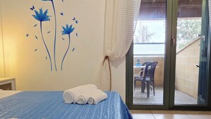 Una habitación con cama, aire acondicionado de pared, ventana con cortina y vista a un patio exterior.
