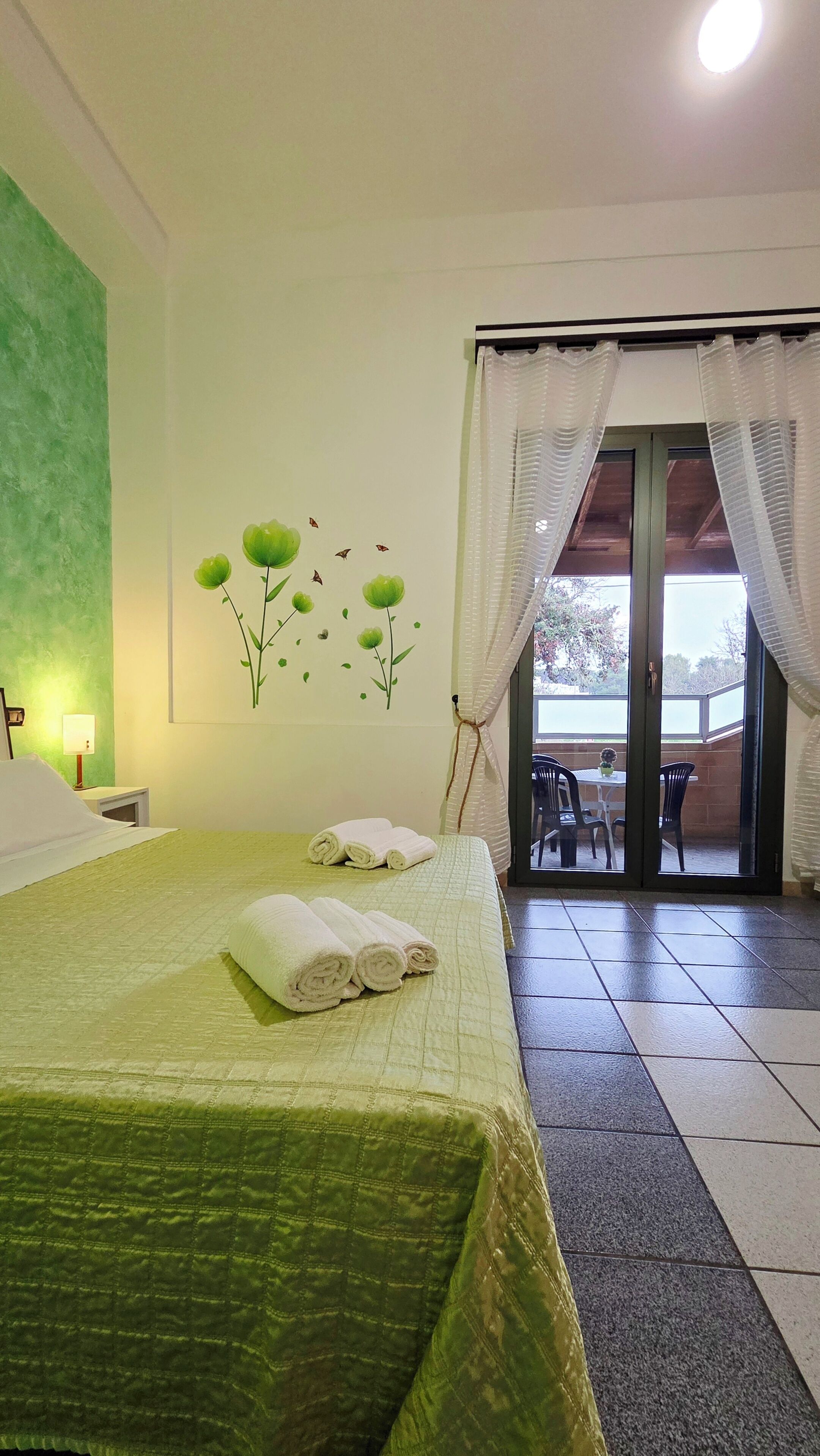 Una camera d'albergo con un letto, un addobbo a parete, una finestra con tende e vista sull'esterno.