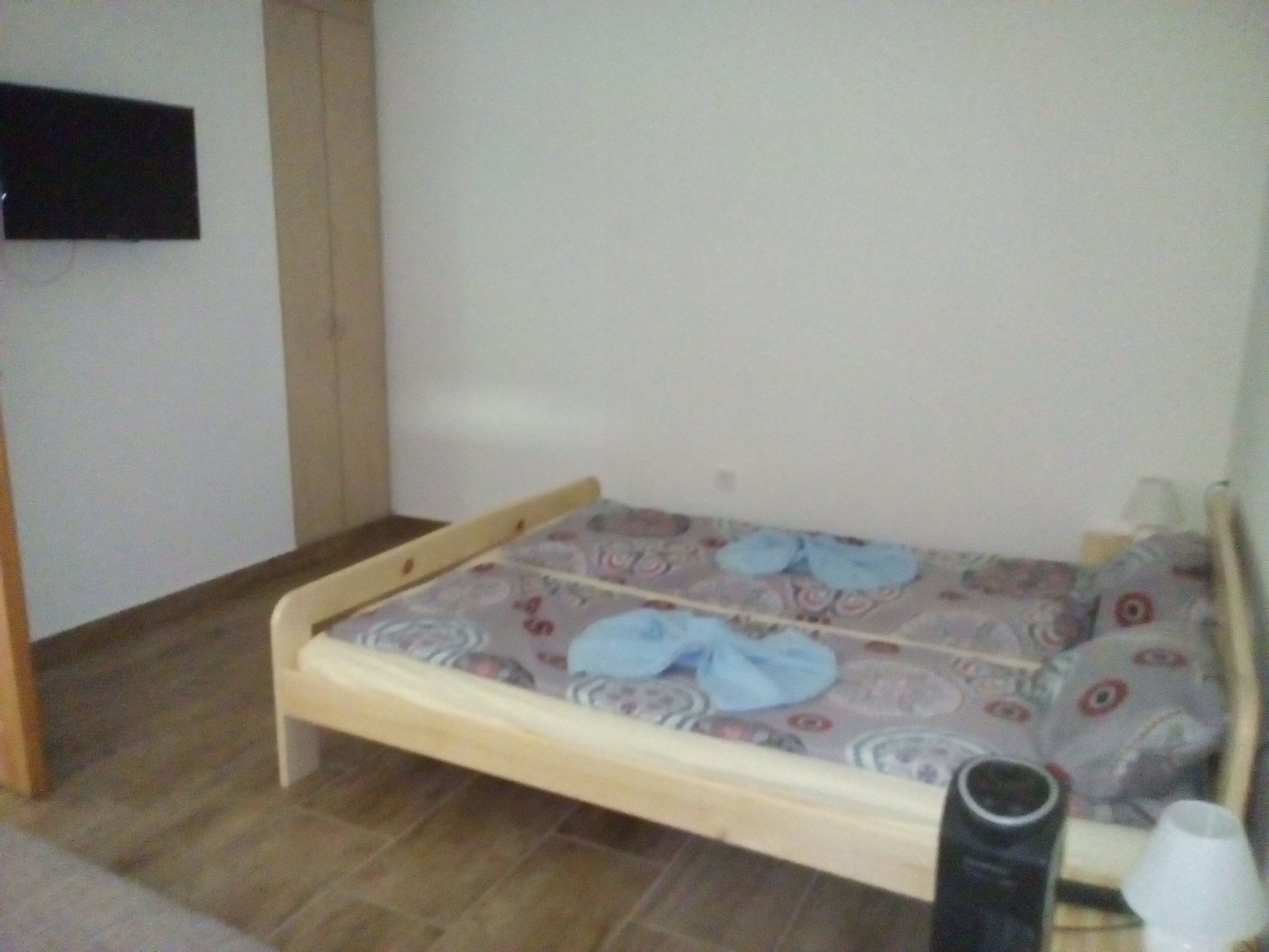 Une petite chambre avec un lit simple, un cadre en bois, un matelas à motifs et un mur uni.