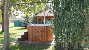 Ein hölzerner Whirlpool in einem Garten mit einer Pergola im Hintergrund.