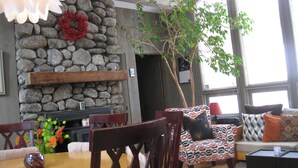 Un salon chaleureux avec une cheminée en pierre, des fauteuils confortables et une grande fenêtre.