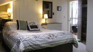 Un lit bien fait, recouvert d’une couvre-lit à motifs, une table de chevet avec une lampe et une commode avec un miroir.