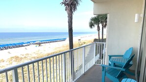 A balcony with two turquoise Adirondack chairs, a white railing, and a view of the beach and ocean.