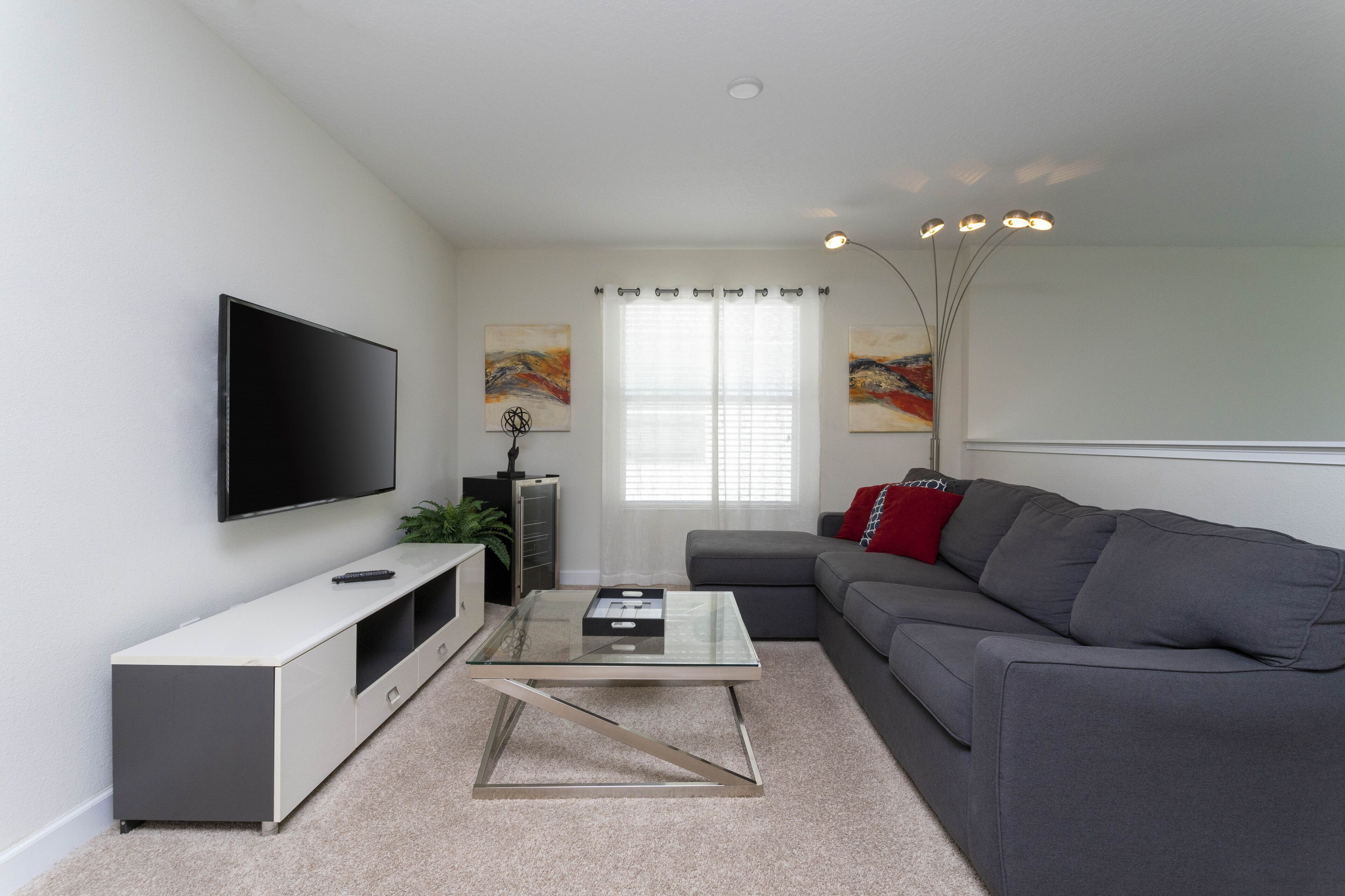 Una sala de estar moderna con un televisor de pantalla plana, una mesa de centro de vidrio, un sofá gris y un mueble blanco para entretenimiento.