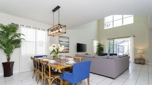 A modern living room with a dining area, a grey sofa, a TV, and a large window. - Single Family Home @ Storey Lake Resort Vacation Homes in Kissimmee...!!! (Kissimmee)