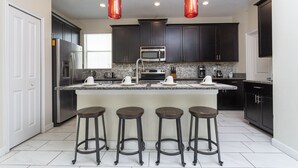 A modern kitchen with dark cabinets, stainless steel appliances, a granite countertop, and four stools. - Single Family Home @ Storey Lake Resort Vacation Homes in Kissimmee...!!! (Kissimmee)