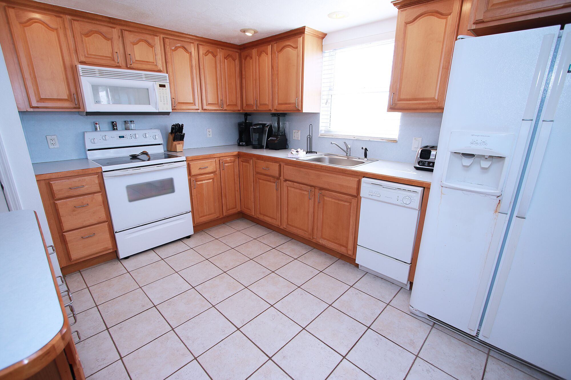 Una cocina con armarios de madera, estufa blanca, microondas, lavavajillas y refrigerador.
