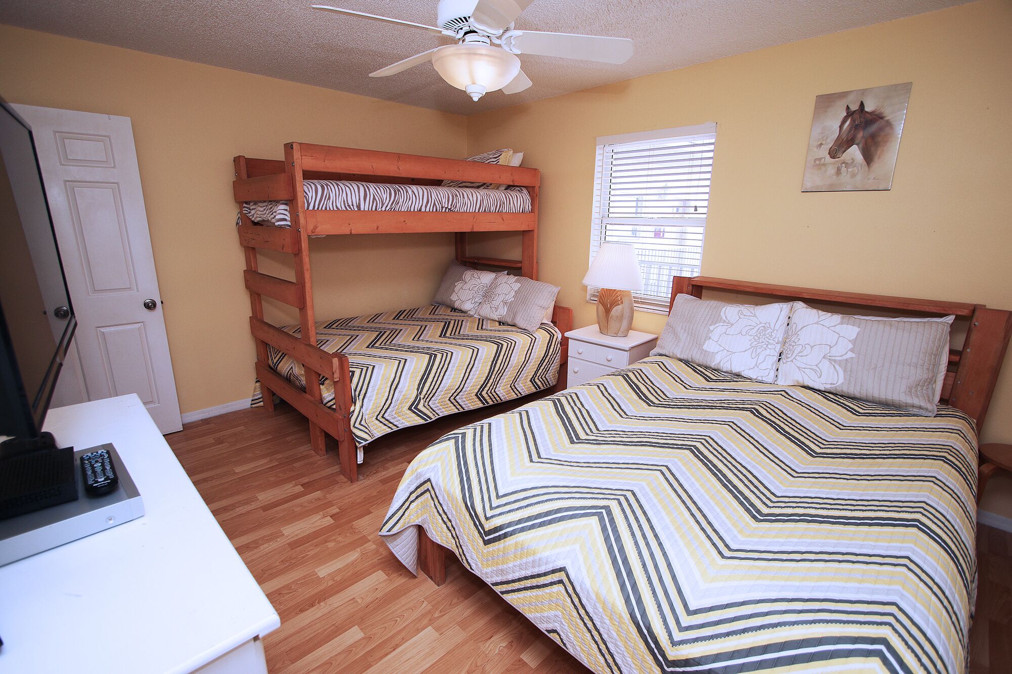 A bedroom with two bunk beds, a desk with a computer, a ceiling fan, and a window with blinds.